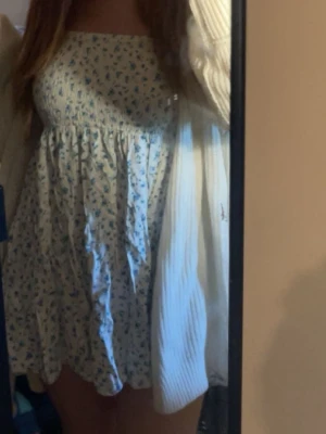 Blommig kortklänning med smock - PASSAR XS OCKSÅ!!!Söt kortklänning med smock upptill och volangig kjol. Klänningen är vit med små blå blommor och har en luftig passform. Perfekt för varma dagar och har en romantisk känsla.