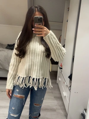 Vit stickad tröja med fransar - Trendig vit stickad tröja med grov ribbstickning och långa ärmar. Nederkanten har snygga fransdetaljer som ger en cool touch. Perfekt att styla med jeans för en avslappnad look. Kolla sista bilden, köptes så. Oanvänd