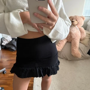 Svart minikjol med volangkant - Säljer en svart kortkjol med volangkant längst ner. Kjolen har en tight passform och är enkel men ändå snygg, perfekt att matcha med olika toppar. Materialet känns mjukt och stretchigt, troligen bomull eller polyester.