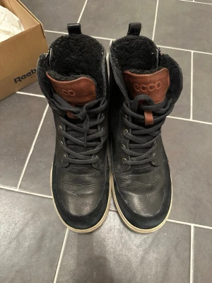 Ecco Kängor Svart Storlek 38 - Snygga svarta stövletter från ECCO med snörning och bruna detaljer vid plösen. Skorna har en robust sula och är fodrade med mjukt svart material för extra värme. Perfekta för kyligare dagar och har en modern, urban look.
