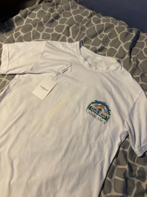 Vit t-shirt från Casablanca - Säljer en vit t-shirt från Casablanca med ett färgglatt broderat motiv och logga på bröstet. Klassisk passform och rund halsringning. Perfekt för dig som gillar stilrena plagg med en twist. Materialet är mjuk bomull som känns skönt mot huden.