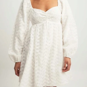 Vit blommig kortklänning från NA-KD - Supersöt vit kortklänning från NA-KD med blommigt mönster och puffiga långärmar. Perfekt inför studenten eller midsommar. Kom tyvärr ej till användning vid min student för hade så många att välja på ;) Hör av dig vid frågor!