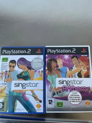Singstar & Singstar Anthems PS2 spel - Två PlayStation 2-spel: Singstar och Singstar Anthems. Båda har färgglada omslag med tecknade figurer och partytema. Perfekt för karaoke och musikälskare, med originalhits och roliga utmaningar. Spelen levereras i plastfodral.