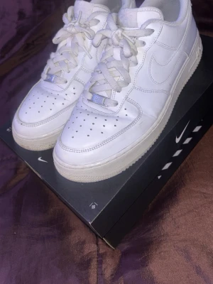 Nike Air Force 1 vita sneakers - Klassiska vita Nike Air Force 1 sneakers i läder med perforerad tå, tjock sula och ikonisk Swoosh-logga på sidorna. Skorna har vita skosnören och diskreta detaljer i silver på snörningen. Perfekt för dig som gillar en clean och tidlös stil. Skorna är använda i drygt ett år, storleken är 44 men passar 43 också. Pris kan diskuteras 