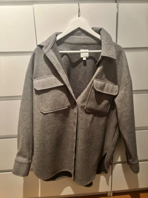Grå kappa - En fin grå kappa med två fickor. Inte använd mycket och där av mycket fint skick. Den har knappar hela vägen. 