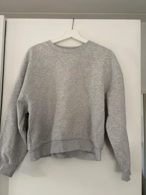Grå basic sweatshirt - En enkel och stilren grå sweatshirt med rund halsringning och långa ärmar. Tröjan har en avslappnad passform och ribbade muddar vid ärmslut och nederkant. Perfekt för en casual look och lätt att matcha med andra plagg.