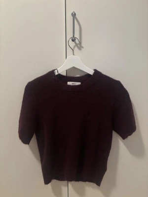 Vinröd stickad topp från Gina Tricot - Mysig vinröd stickad topp från Gina Tricot i alpackablandning. Modellen har korta ärmar, rund halsringning och en något croppad passform. Perfekt för lager-på-lager och en trendig look. Pris kan diskuteras 