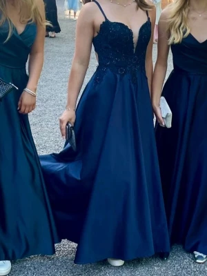 Marinblå balklänning med spetsdetaljer och öppen rygg - Jättefin mörkblå balklänning med spetsdetaljer och öppen rygg. Klänningen har smala axelband och en v-ringad urringning. Jag är 165 och den var perfekt med ett par sneakers💗är köpt från JJs house ursprungspris 1999kr