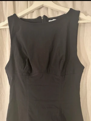 Svart ärmlös kortklänning - En klassisk svart kortklänning med figurnära passform och rund halsringning. Klänningen är ärmlös och har dragkedja i ryggen. Perfekt basplagg som kan stylas på många olika sätt.