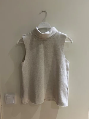 Beige stickad väst från Zara - Säljer en beige stickad polo tröja från Zara. Tröjan är ärmlös och har en mjuk, ribbad struktur som ger en clean och modern look. Säljer då den tyvärr blivit för liten för mig. Pris kan diskuteras