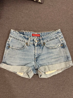 Ljusblå jeansshorts från Indian Rose - Snygga ljusblå jeansshorts från Urban Rose med klassisk femficksdesign, uppvikta benslut och knappgylf. Shortsen har bälteshällor och detaljerade sömmar både fram och bak. Perfekta för varma dagar och enkel att matcha med olika stilar.