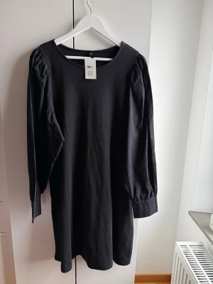 Ny Kappahl svart klänning, storlek L - Ny Kappahl svart klänning, storlek L  _Svart klänning med långa ärmar.  -Ärmarna har puffdetaljer vid axlarna och manschetter med dekorativa knappar.  -Ny med prislappen kvar. Mycket fin.  🚭Djurfritt och rökfritt hem 🌸Se gärna mina andra annonser för samfrakt ✨Har bundle-rabatt