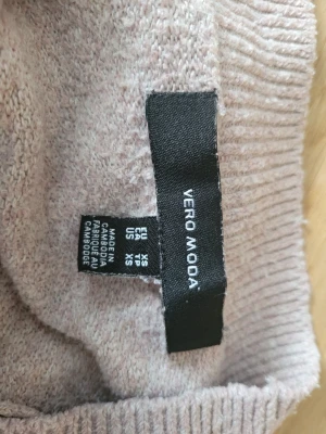 Ljusbeige stickad tröja Vero Moda - Mysig ljusbeige stickad tröja från Vero Moda. Tröjan har en enkel design med ribbstickad kant vid halsringning och nederkant. Perfekt för lager på lager och passar till det mesta i garderoben.