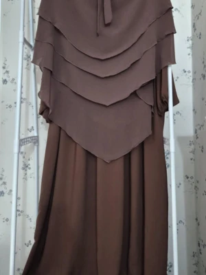 Abaya med khimar  - Två eleganta långklänningar med lager på lager-design och slöja. En i mörkbrun och en i marinblå färg. Klänningarna har löst fall och är tillverkade i ett lätt, flytande material som ger en snygg siluett. Perfekt för dig som gillar modest och stilren look.