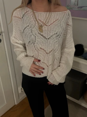 Vit stickad tröja med hålmönster - Säljer en vit stickad tröja med snyggt hålmönster och bred halsringning som kan bäras off-shoulder. Tröjan har långa ärmar och en avslappnad passform, perfekt att styla med kedjor och svarta byxor. Materialet känns mjukt och luftigt.