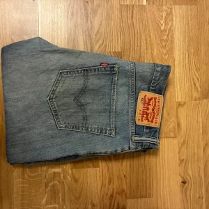 Levi's 511 ljusblå jeans - Säljer ett par klassiska Levi's 511 jeans i ljusblå denim. Modellen har raka ben, fem fickor och ikonisk läderpatch bak i midjan. Snygg tvättad look och diskreta slitningar. Perfekta för en avslappnad stil.