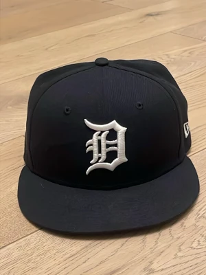 Svart Detroit Tigers keps New Era fitted cap - Snygg svart keps från New Era med Detroit Tigers-logga broderad i vitt framtill. Klassisk flat brim och broderad MLB-logga baktill. Perfekt för dig som gillar streetwear och sportig stil.