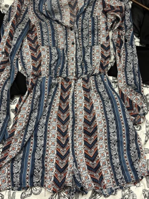 Mönstrad långärmad jumpsuit - Säljer en långärmad jumpsuit med blå, vita och röda inslag. Jumpsuiten har ett detaljerat randigt och geometriskt mönster, knappar framtill och resår i midjan för en bekväm passform. Perfekt för dig som gillar boho-vibbar och snygga detaljer. Kort klänning med shorts