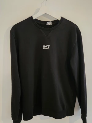 Svart sweatshirt från Emporio Armani - Säljer en svart sweatshirt från Emporio Armani EA7 med rund halsringning och diskret logga på bröstet. Storlek L men liten i storlek passar M/S bättre 
