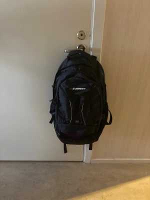 Svart ryggsäck från Everest - Rymlig svart ryggsäck från Everest med flera fack och justerbara axelband. Tillverkad i slitstarkt material och har en sportig design med logga framtill. Perfekt för skola, träning eller utflykter. Använd endast 1 gång