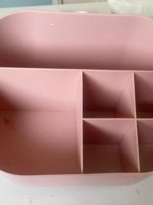 Rosa sminkorganiserare i plast - Praktisk rosa sminkorganiserare i plast med flera fack i olika storlekar. Perfekt för att hålla ordning på sminkborstar, pennor och andra skönhetsverktyg. Modern och stilren design med rundade hörn.