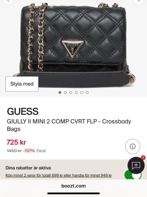 Svart quiltad axelväska från Guess - Snygg svart axelväska från Guess i quiltat mönster med guldfärgade kedjedetaljer och logga framtill. Väskan har en kompakt design med lock och justerbar axelrem. Perfekt för att bära det viktigaste med stil.