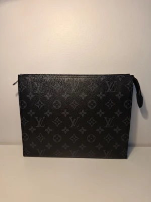 LoV svart Monogram clutch - Stilren svart clutch från LoV  med klassiskt monogrammönster i grått. Väskan är rektangulär med dragkedja upptill och tillverkad i läder. Perfekt för att bära det viktigaste och ger en lyxig touch till din outfit.