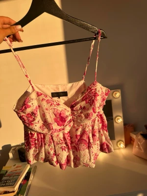 Blommig rosa linnetopp från Zara - Supersöt linnetopp från Zara med tunna axelband och blommigt mönster i rosa och vitt. Toppen har broderade detaljer och lätt volang nedtill för en romantisk vibe. Perfekt för varma dagar och somriga outfits!