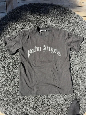Svart Palm Angels t-shirt - Svart t-shirt från Palm Angels med klassisk logga i vitt på bröstet. T-shirten har rund halsringning och korta ärmar. Perfekt för dig som gillar streetwear och vill ha en stilren look.