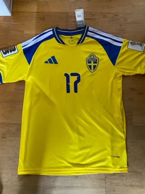 Sverige fotbollströja Gyökeres 17 - Gul och blå Sverige fotbollströja med nummer 17 och namnet Gyökeres på ryggen. Tröjan har blå detaljer, broderad landslagssköld och tryckta loggor på ärmarna. Tillverkad i funktionsmaterial för sport.                             Går att hämta i person!                                      Hör gärna av er med evt frågor 😁
