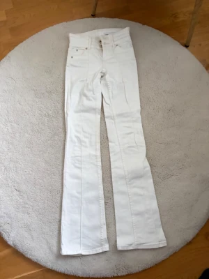 Vita utsvängda jeans med låg midja  - Säljer ett par vita jeans med låg midja och utsvängda ben. Klassisk femficksmodell med knappgylf och raka sömmar. Perfekta för dig som vill ha en clean och trendig look. Materialet ser ut att vara bomull med lite stretch.
