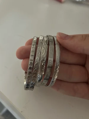 Silverfärgade armband med mönster - Säljer ett set med fem silverfärgade armband i metall. Armbanden har olika ingraverade mönster och detaljer, vissa med små kulor i ändarna. Perfekta för att mixa och matcha till din stil. Snygga att bära både tillsammans eller var för sig.