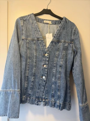 Ljusblå jeansjacka från Perfect Jeans - Trendig ljusblå jeansjacka från Perfect Jeans med V-ringning och fyra knappar framtill. Jackan har markerade sömmar, utsvängda ärmar och en avslappnad passform. Perfekt för dig som vill ha en unik twist på den klassiska jeansjackan.