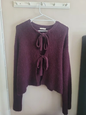 Vinröd kofta med knytband - Mysig vinröd kofta i fluffigt stickat material med två dekorativa knytband framtill. Koftan har lång ärm och rak passform, perfekt för lager på lager och en trendig look. Enkel att styla till både jeans och kjol.