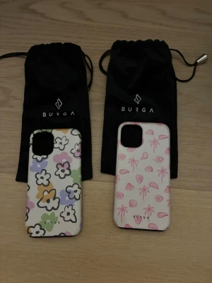 Två BURGA mobilskal - Säljer två mobilskal till iPhone 12 Mini(passar till 13 Mini oxå) från BURGA. Båda är hårda skal i plast och kommer med svarta tygpåsar. Osynliga små repor på båda och en synlig repa på de rosa(bild 3) 150kr styck 250 för båda, kan ändra pris oxå