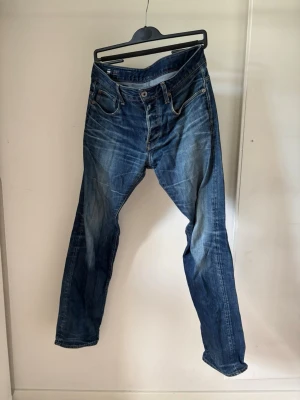 G star 3301 Straight - Snygga blå jeans med raka ben och coola slitningar på både fram- och baksida. Klassisk femficksmodell med knappgylf och kontrastsömmar. Jeansen är i denim och har en avslappnad passform som funkar till det mesta.