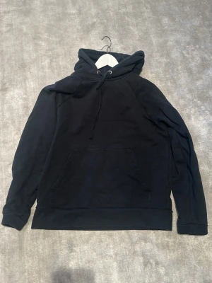 Svart a days march hoodie - En klassisk svart hoodie med huva och dragsnören. Hoodien har en stor magficka framtill och ribbade muddar vid ärmslut och nederkant. Tillverkad i mjukt bomullsmaterial, perfekt för en avslappnad och stilren look. Strlk m passar s