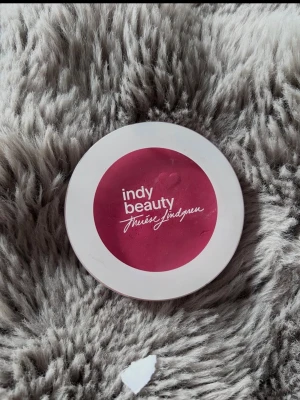 Indy Beauty rouge i rosa nyans - Rouge från Indy Beauty i en rund vit dosa med rosa lock och logotyp. Färgen är en djup rosa ton som ger kinderna ett fräscht och naturligt glow. Perfekt för att framhäva ansiktets konturer och skapa en pigg look.