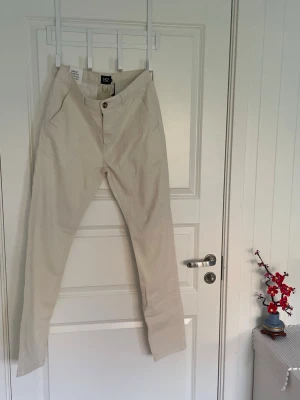 Beige chinos med raka ben - Snygga beige chinos med raka ben och klassisk passform. Byxorna har två sidofickor och stängs med knapp och dragkedja. Tillverkade i ett mjukt bomullstyg som känns bekvämt hela dagen. Perfekta för en clean och stilren look.