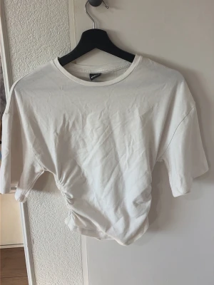 Vit croppad t-shirt  - Säljer en vit croppad t-shirt som är indragen vid magen o midjan för en tajt look
