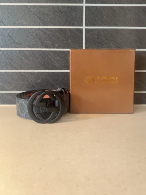 Svart bälte med GG-spänne - Snyggt svart bälte med klassiskt GG-mönster och stort matt svart GG-spänne. Bältet har en stilren design och passar perfekt till jeans eller byxor för en trendig look. Kommer med originalask.