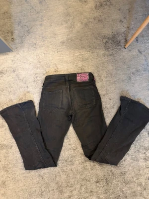 Svarta bootcut jeans från Cheap Monday - Säljer ett par svarta bootcut jeans från Cheap Monday med klassisk femficksmodell och en lila logga bak i midjan. Jeansen har låg midja och är tillverkade i stretchigt denimtyg för en bekväm passform. Perfekta för dig som gillar en retro vibe. Lite slitningar längst ner vid hälarna men inget som syns med dom på!