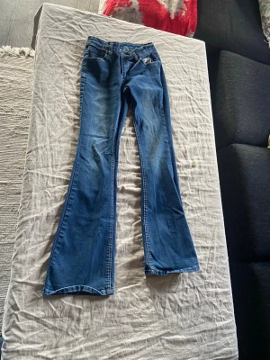 Blå bootcut jeans med utsvängda ben - Säljer ett par klassiska blå bootcut jeans med utsvängda ben och fem fickor. Jeansen har en snygg tvätt med lätt slitning framtill och baktill. Perfekta för dig som gillar retrostil och vill ha ett par jeans med skön passform.