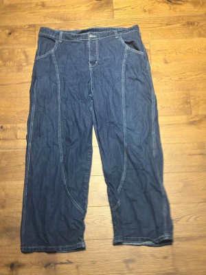Blå baggy jeans - Säljer ett par blå baggy jeans med tydliga kontrastsömmar och avslappnad passform. Jeansen har klassiska fickor fram och bak samt raka ben. Perfekta för en chill och avslappnad stil.