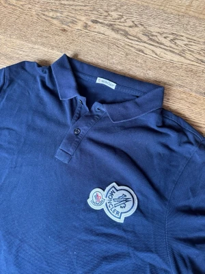 Moncler double logo piké - Säljer en moncler double logo pike som är i bra skick lite urtvättad och två små prickar/hål men inget som man lägger märke till.  Storlek är Large