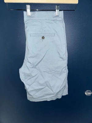 Ljusblå bomullsshorts med fickor - Snygga ljusblå shorts i bomull med klassisk passform. Shortsen har två sidofickor och en bakficka med knapp. Perfekta för varma dagar och enkel att matcha med olika stilar.