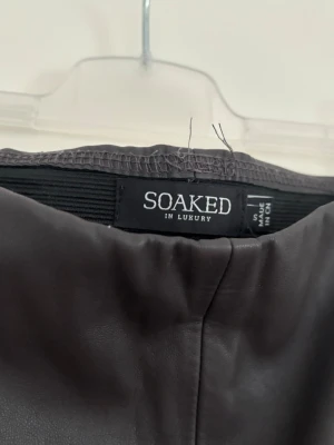 Svarta skinnbyxor från Soaked in Luxury - Säljer ett par svarta skinnbyxor från Soaked in Luxury. Byxorna har hög midja, raka ben och resår i midjan för extra komfort. Snygg minimalistisk look som passar till många olika stilar. Materialet är mjukt och följsamt.