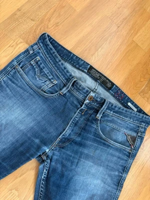 Blå jeans från Replay - Säljer ett par klassiska blå jeans från Replay med snygg tvätt och raka ben. Jeansen har fem fickor, detaljerade sömmar och Replay-logga på bakfickan. Perfekta för dig som gillar en avslappnad men stilren look. Stil: Anbass med storlek 33 