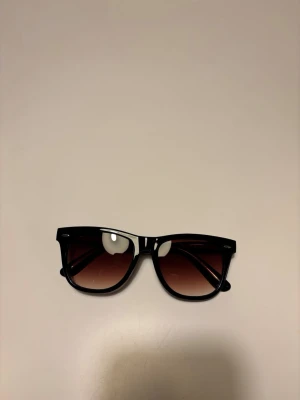 Raybans solglasögon liknande - Snygga solglasögon med svart båge och bruna tonade glas. Klassisk och stilren design som passar till de flesta outfits. Perfekta för soliga dagar och ger en cool vibe.