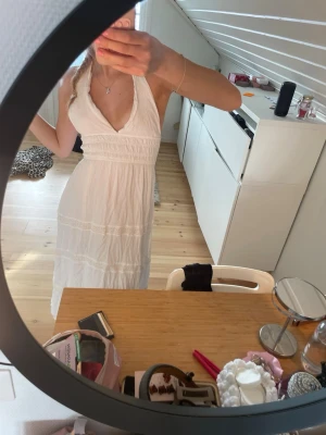 Vit långklänning med halterneck - Säljer en vit långklänning med halterneck och öppen rygg. Klänningen har v-ringad urringning, fina spetsdetaljer och knyt i nacken. Perfekt för sommaren och ger en romantisk vibe. Jag är 168 och den är nästan ner till fötterna på mig, skulle passa perfekt om man är lite kortare skulle jag säga. Använd 1 gång.